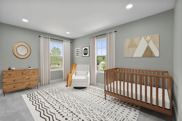 carpeted bedroom with recessed lighting, multiple windows, and a crib