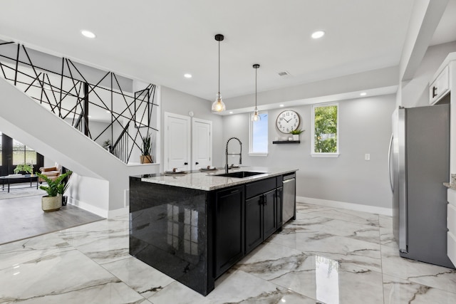 kitchen featuring marble finish floor, a center island with sink, stainless steel appliances, a sink, and dark cabinetry