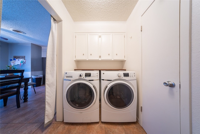 laundry room with washing machine and dryer, a textured ceiling, and cabinets