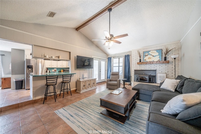 living area with a ceiling fan, a textured ceiling, visible vents, lofted ceiling with beams, and light tile patterned flooring