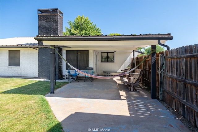 back of house featuring a chimney, a lawn, brick siding, fence, and a patio