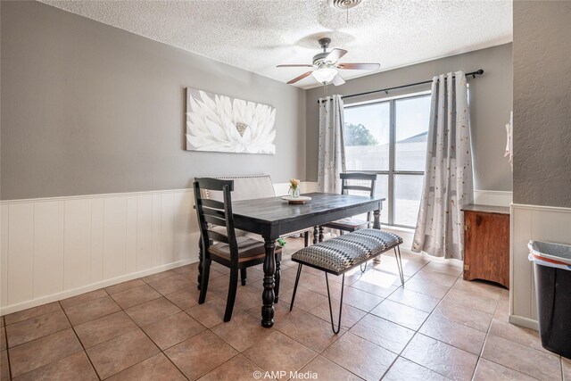 tiled dining room with a textured ceiling, ceiling fan, and a wainscoted wall