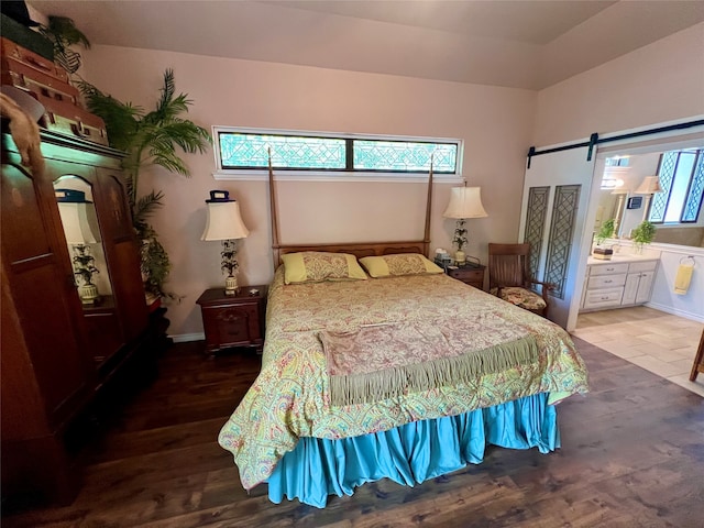 bedroom featuring connected bathroom, a barn door, and wood-type flooring