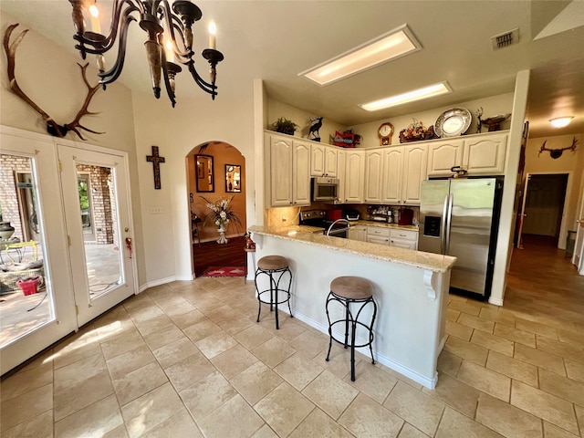 kitchen featuring a kitchen breakfast bar, kitchen peninsula, white cabinetry, a chandelier, and appliances with stainless steel finishes