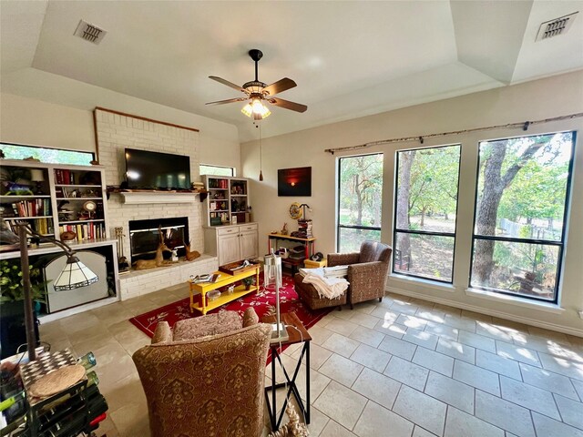 tiled living room featuring ceiling fan, a tray ceiling, and a brick fireplace