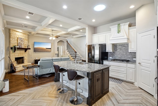 kitchen with beam ceiling, white cabinets, stainless steel appliances, coffered ceiling, and a stone fireplace