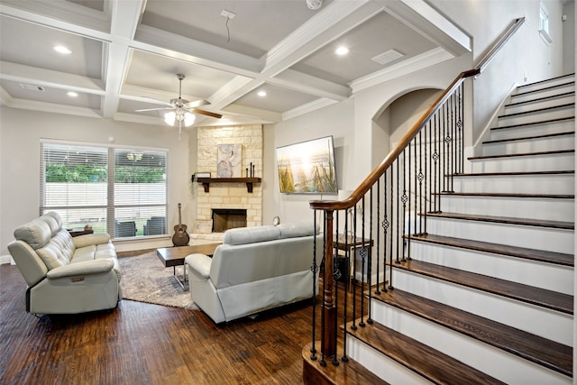 living room featuring beamed ceiling, hardwood / wood-style flooring, a stone fireplace, ceiling fan, and coffered ceiling