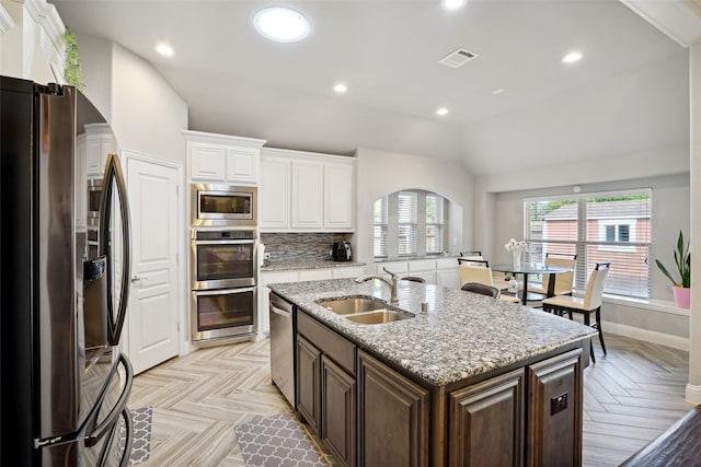 kitchen with stainless steel appliances, light parquet flooring, an island with sink, sink, and backsplash