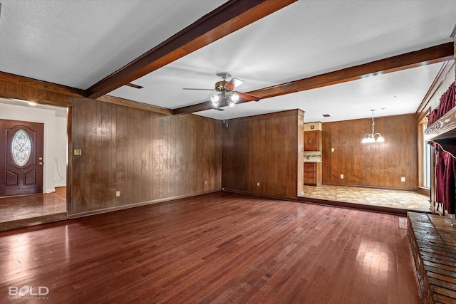 unfurnished living room with ceiling fan with notable chandelier, dark hardwood / wood-style floors, beamed ceiling, and wooden walls