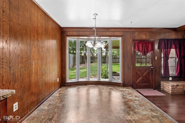 unfurnished dining area with a chandelier, wooden walls, and ornamental molding