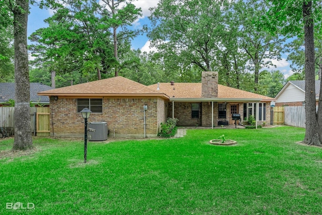 rear view of house with a fire pit, a lawn, and central AC