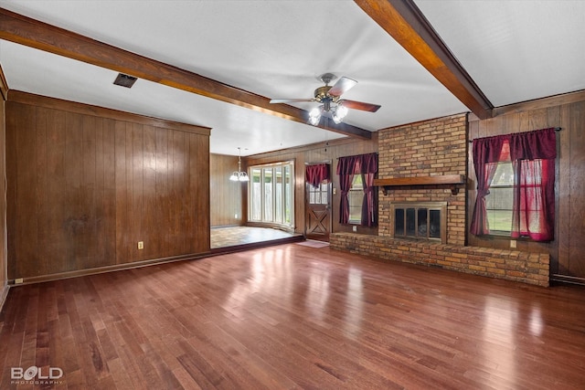 unfurnished living room featuring beamed ceiling, a brick fireplace, dark hardwood / wood-style flooring, ceiling fan, and wood walls