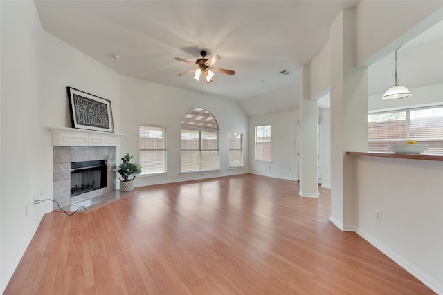 unfurnished living room with light hardwood / wood-style floors, a tiled fireplace, ceiling fan, and lofted ceiling