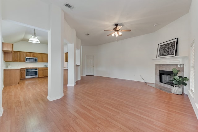 unfurnished living room with ceiling fan, a tiled fireplace, light hardwood / wood-style flooring, and vaulted ceiling