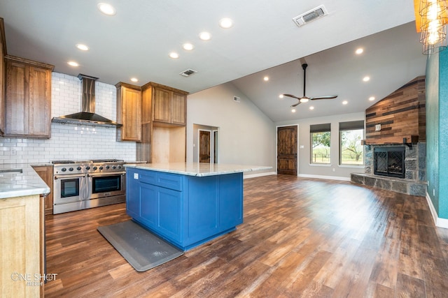 kitchen with wall chimney exhaust hood, a stone fireplace, backsplash, range with two ovens, and a kitchen island