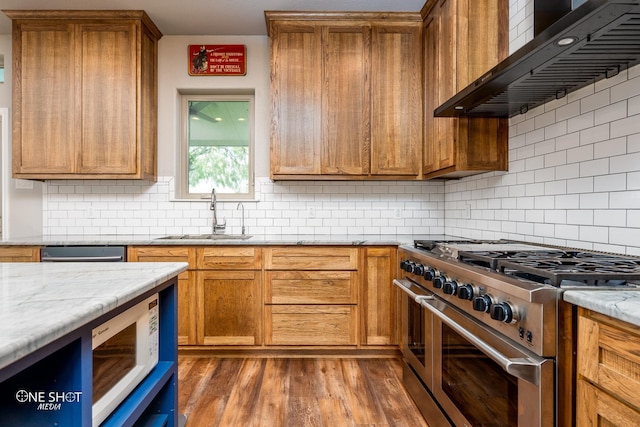 kitchen with appliances with stainless steel finishes, backsplash, light stone counters, wall chimney exhaust hood, and sink