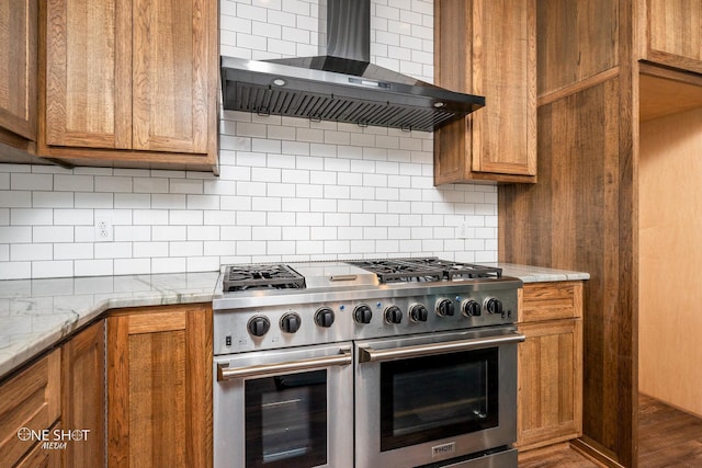 kitchen with light stone countertops, decorative backsplash, double oven range, and wall chimney range hood