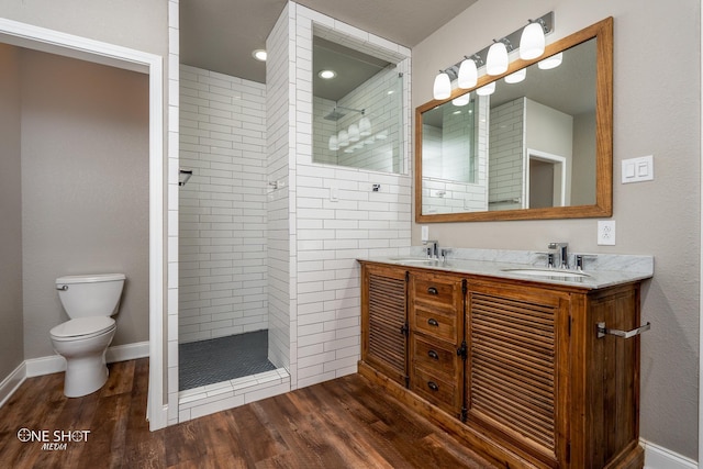 bathroom with a tile shower, hardwood / wood-style floors, vanity, and toilet