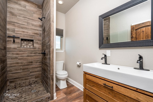 bathroom with tiled shower, vanity, wood-type flooring, and toilet