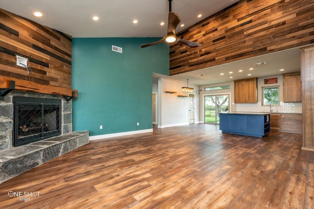 unfurnished living room featuring dark hardwood / wood-style flooring, high vaulted ceiling, a stone fireplace, and ceiling fan