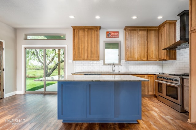 kitchen with wall chimney exhaust hood, light hardwood / wood-style flooring, range with two ovens, decorative backsplash, and a kitchen island