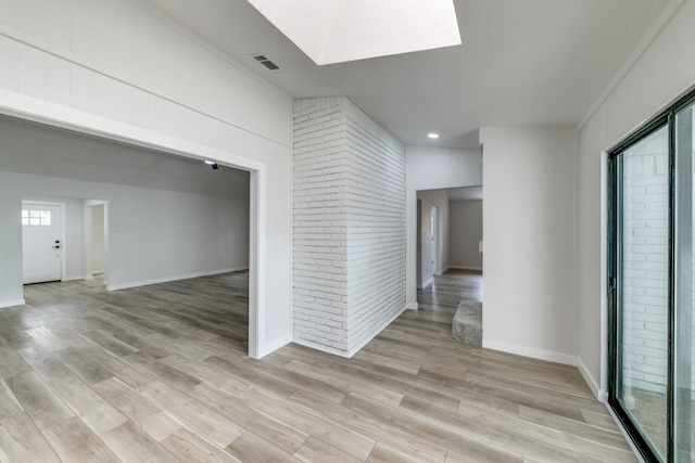 empty room featuring a skylight, light hardwood / wood-style flooring, and brick wall