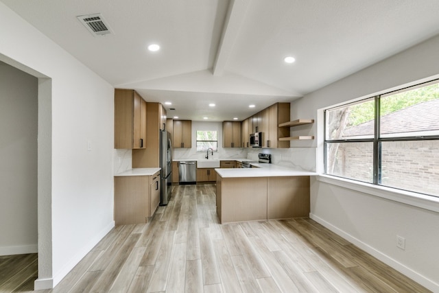 kitchen with light wood-type flooring, lofted ceiling with beams, appliances with stainless steel finishes, kitchen peninsula, and backsplash