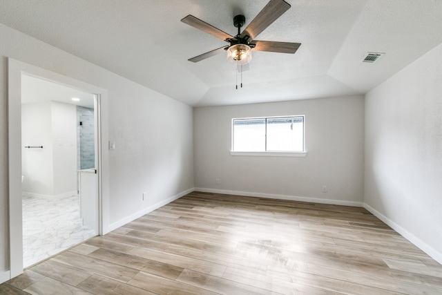 spare room with lofted ceiling, a textured ceiling, light wood-type flooring, and ceiling fan