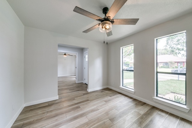 spare room featuring light wood-type flooring, ceiling fan, and a healthy amount of sunlight