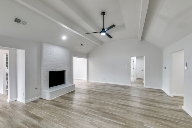 unfurnished living room featuring ceiling fan, brick wall, lofted ceiling with beams, light hardwood / wood-style flooring, and a brick fireplace