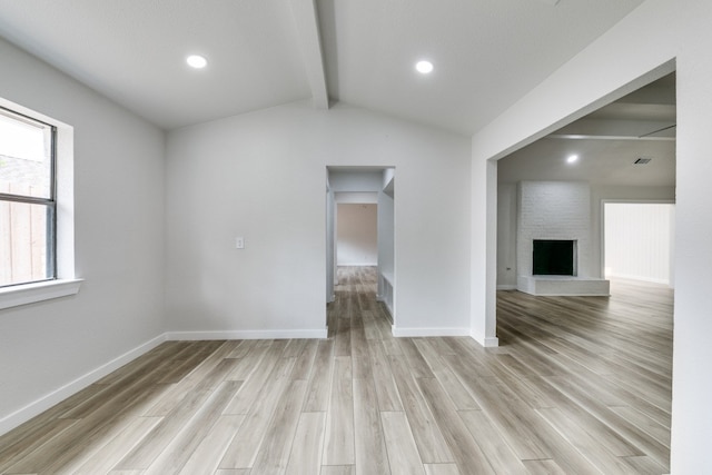 unfurnished living room featuring brick wall, a fireplace, lofted ceiling with beams, and light wood-type flooring