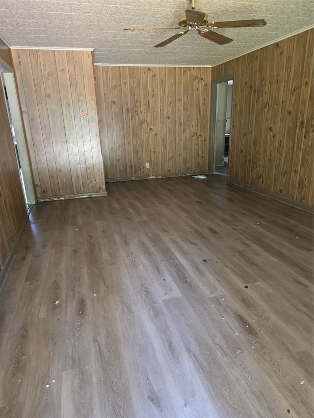 empty room featuring ceiling fan, wood walls, a textured ceiling, and wood-type flooring