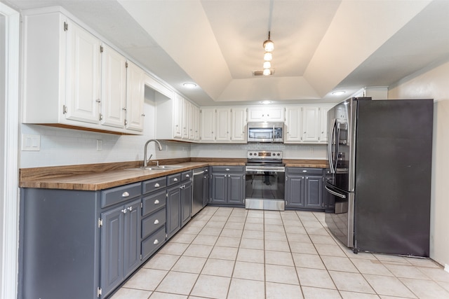 kitchen featuring butcher block countertops, appliances with stainless steel finishes, white cabinets, gray cabinets, and a raised ceiling