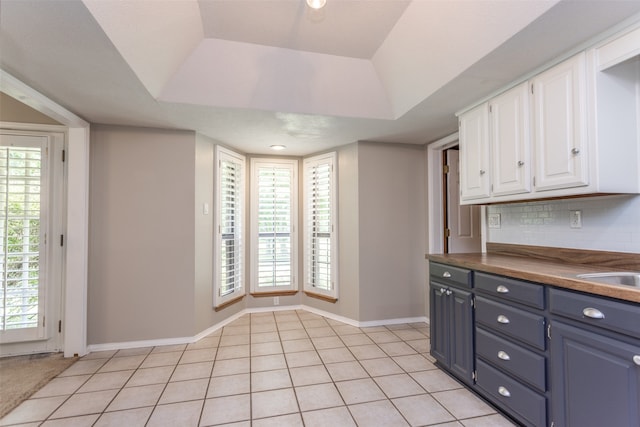 kitchen with white cabinets, a healthy amount of sunlight, tasteful backsplash, and a tray ceiling