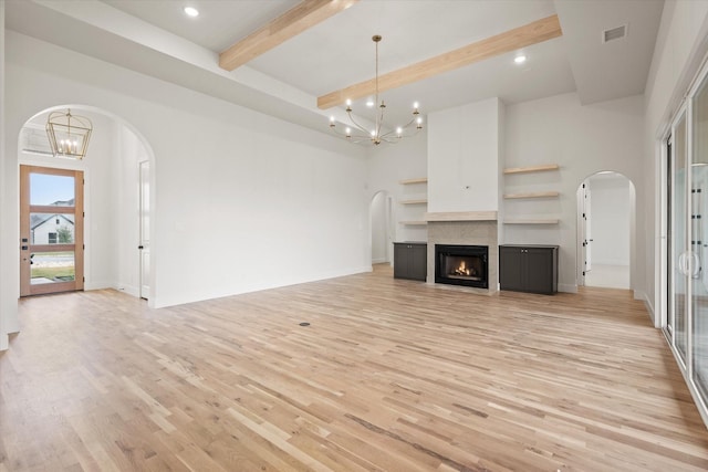 unfurnished living room with an inviting chandelier, a towering ceiling, light hardwood / wood-style floors, and beamed ceiling