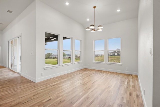 empty room featuring a chandelier, light hardwood / wood-style floors, and a wealth of natural light