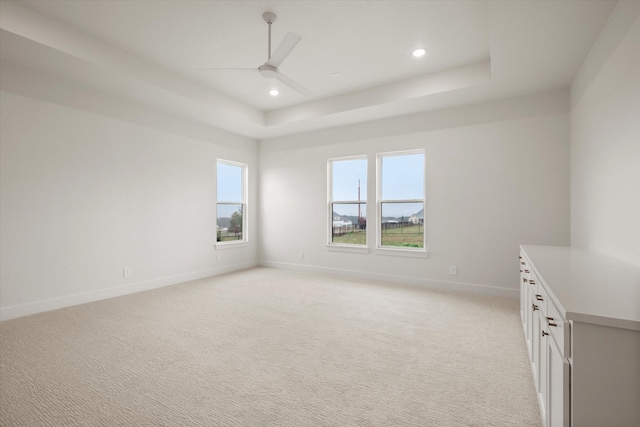 empty room with a raised ceiling, plenty of natural light, light colored carpet, and ceiling fan