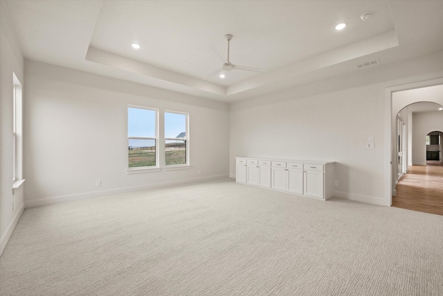 unfurnished room featuring light carpet, a raised ceiling, and ceiling fan