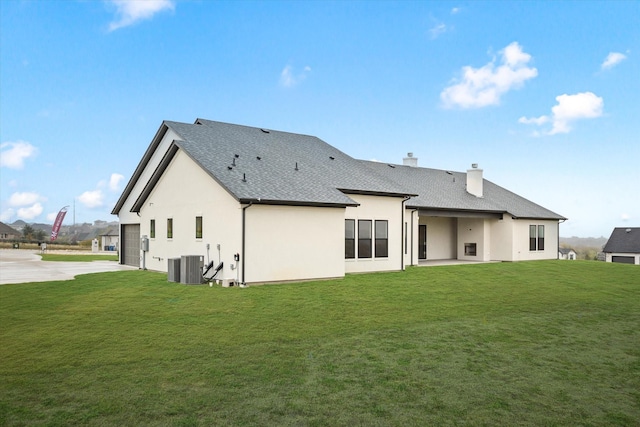 rear view of house with a garage, a yard, and central AC