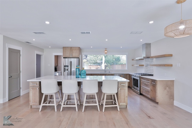 kitchen with wall chimney exhaust hood, a kitchen island, light wood-type flooring, and stainless steel appliances