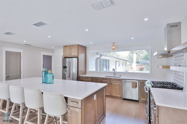 kitchen featuring light wood-type flooring, wall chimney range hood, a kitchen island, high end appliances, and sink