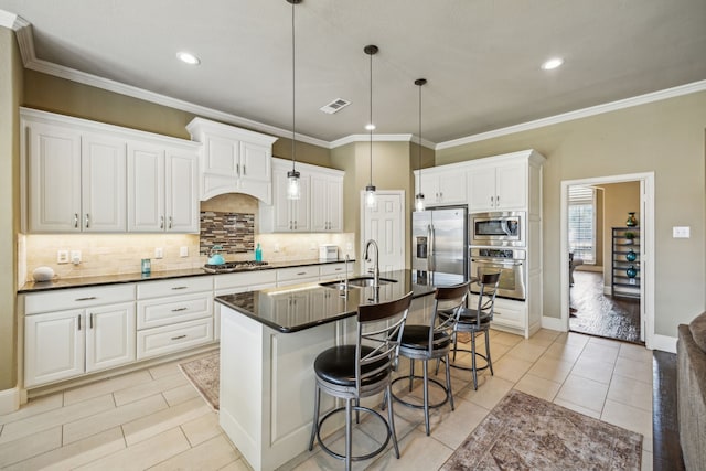 kitchen with sink, hanging light fixtures, a kitchen island with sink, white cabinets, and appliances with stainless steel finishes