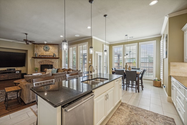 kitchen featuring dishwasher, a stone fireplace, sink, an island with sink, and light tile patterned flooring