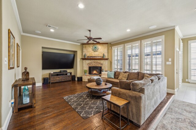 living room with wood-type flooring, a stone fireplace, ceiling fan, and ornamental molding