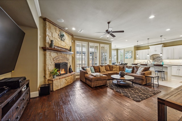 living room with ceiling fan, crown molding, sink, wood-type flooring, and a fireplace