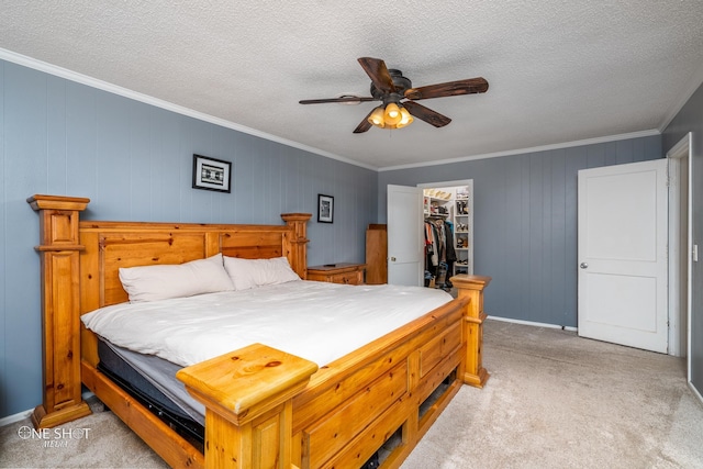 carpeted bedroom with a walk in closet, ornamental molding, a textured ceiling, ceiling fan, and a closet