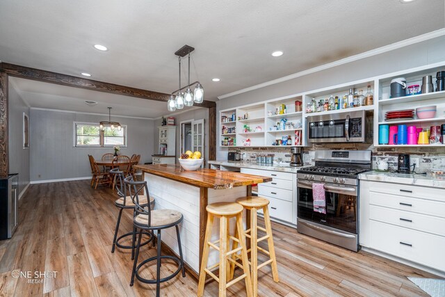 kitchen featuring wood counters, a kitchen breakfast bar, stainless steel appliances, white cabinets, and hanging light fixtures