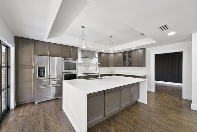 kitchen with pendant lighting, dark hardwood / wood-style flooring, an island with sink, and appliances with stainless steel finishes