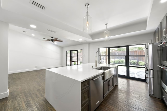 kitchen featuring stainless steel appliances, dark wood-type flooring, sink, pendant lighting, and a center island with sink