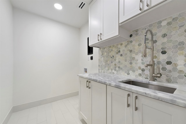 kitchen featuring backsplash, light stone countertops, white cabinetry, and sink